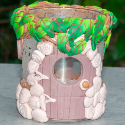 photo of candleholder decorated with a fairy door, little stones, vines, leaves, and even stucco, made from polymer clay